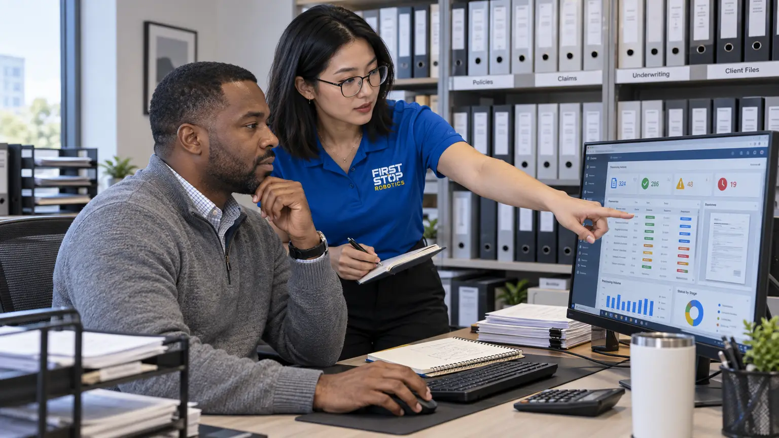 A claims handler at two monitors with a processing dashboard, a First Stop consultant pointing at a flagged item, shelves of binders behind