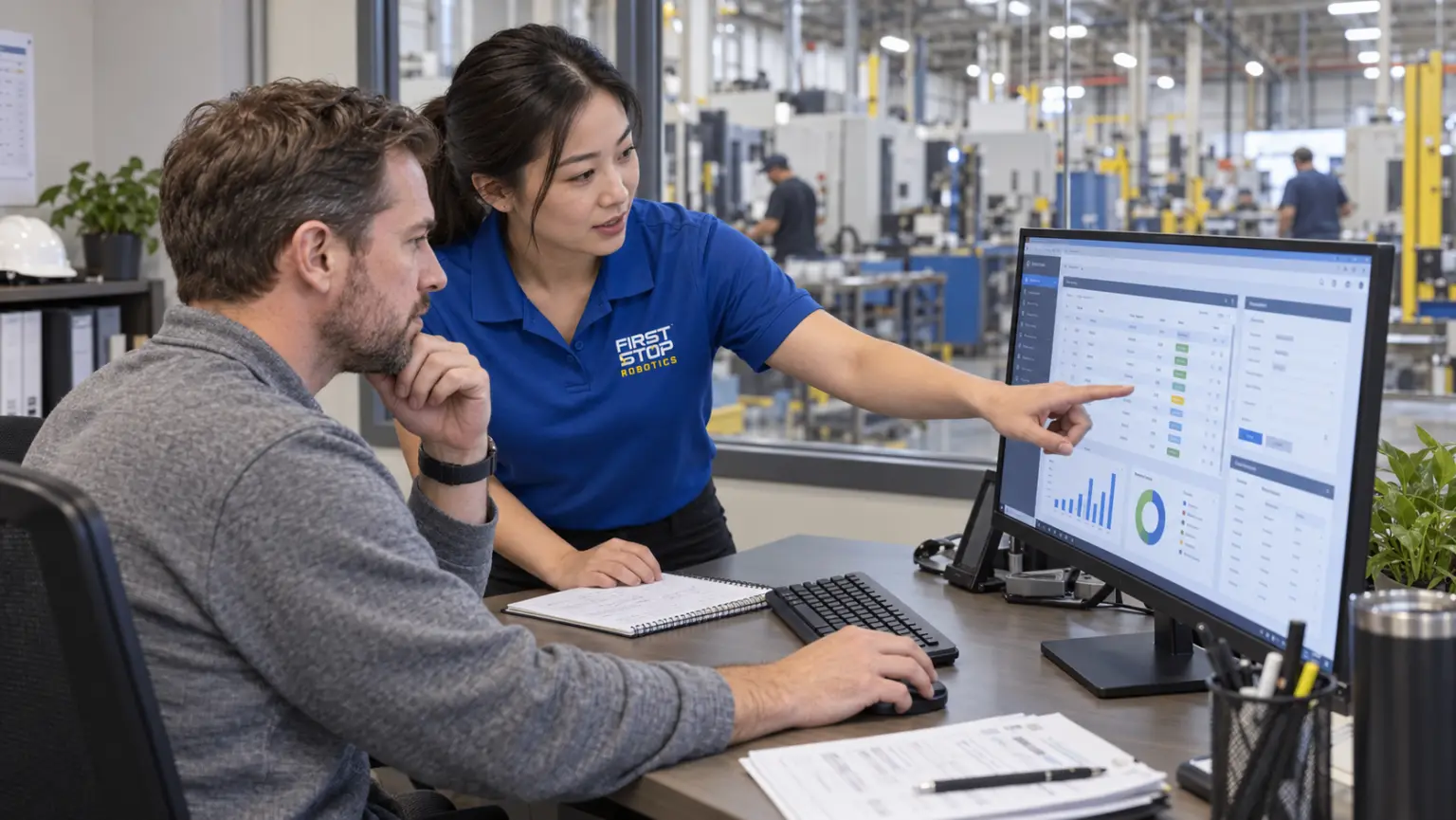 A First Stop consultant pointing at a production dashboard on screen while a plant manager works the mouse and thinks it over, the machining floor behind